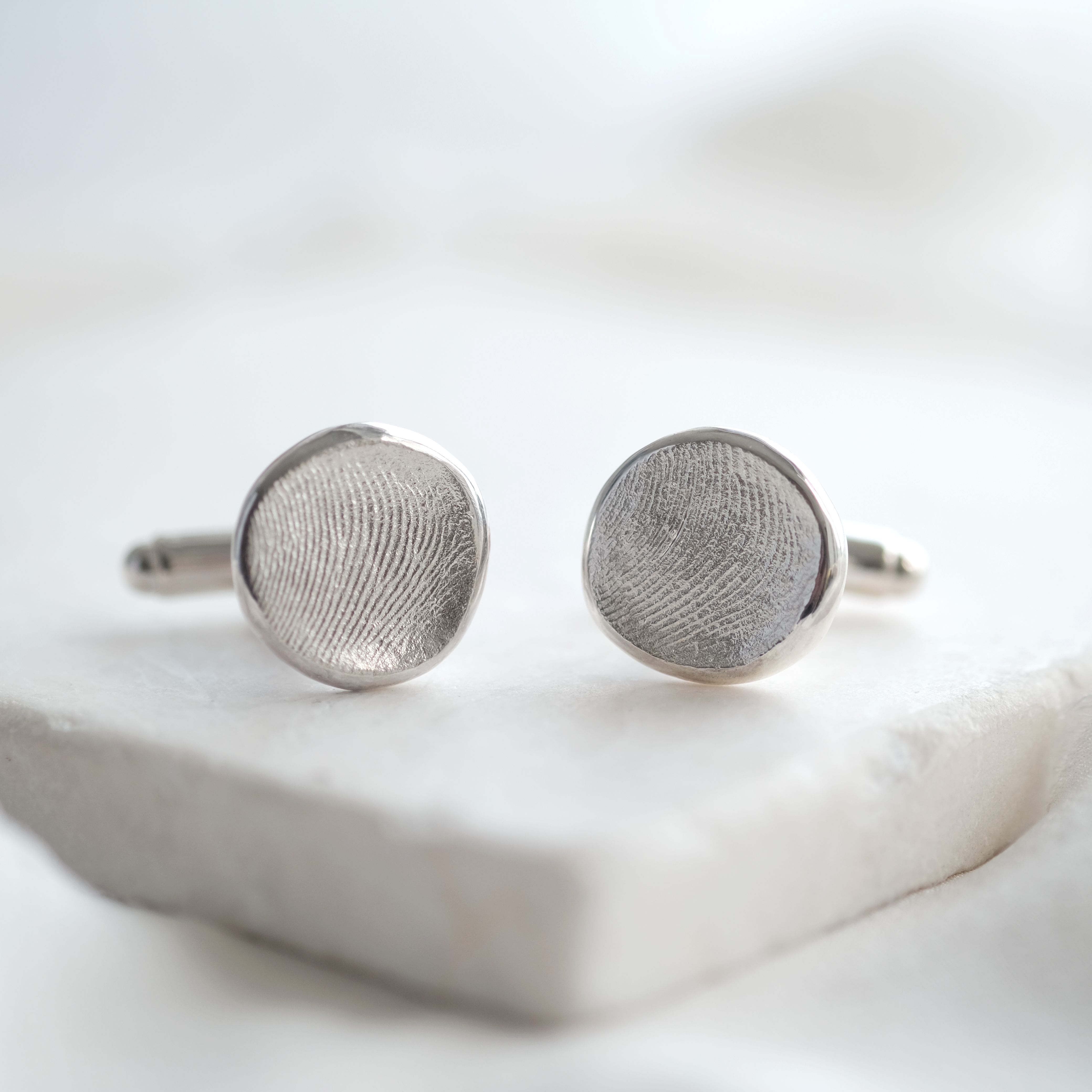 Pair of silver fingerprint cufflinks on a white surface