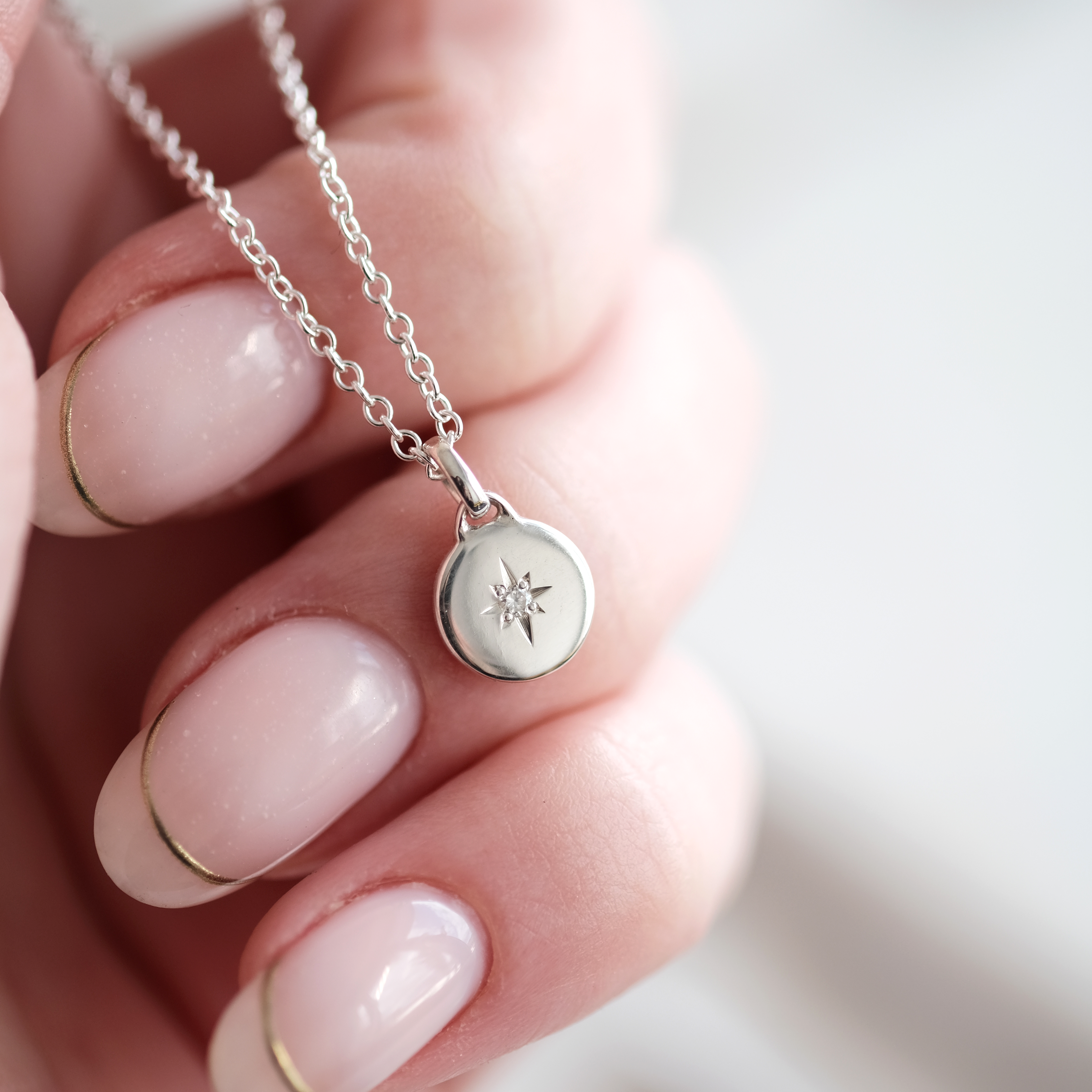 Silver necklace with a star pendant held by a hand against a blurred background