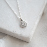 Silver necklace with a round pendant on a light fabric background